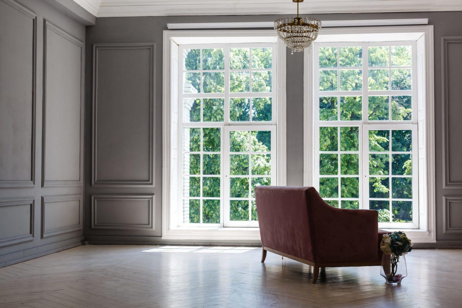 White room with pink sofa-bed, flowers in glass jug and mirror near the window. Classic interior design